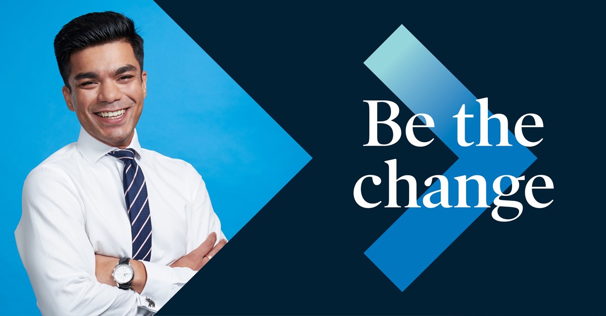 Man in business attire facing the camera. Text on banner is "Be the change"